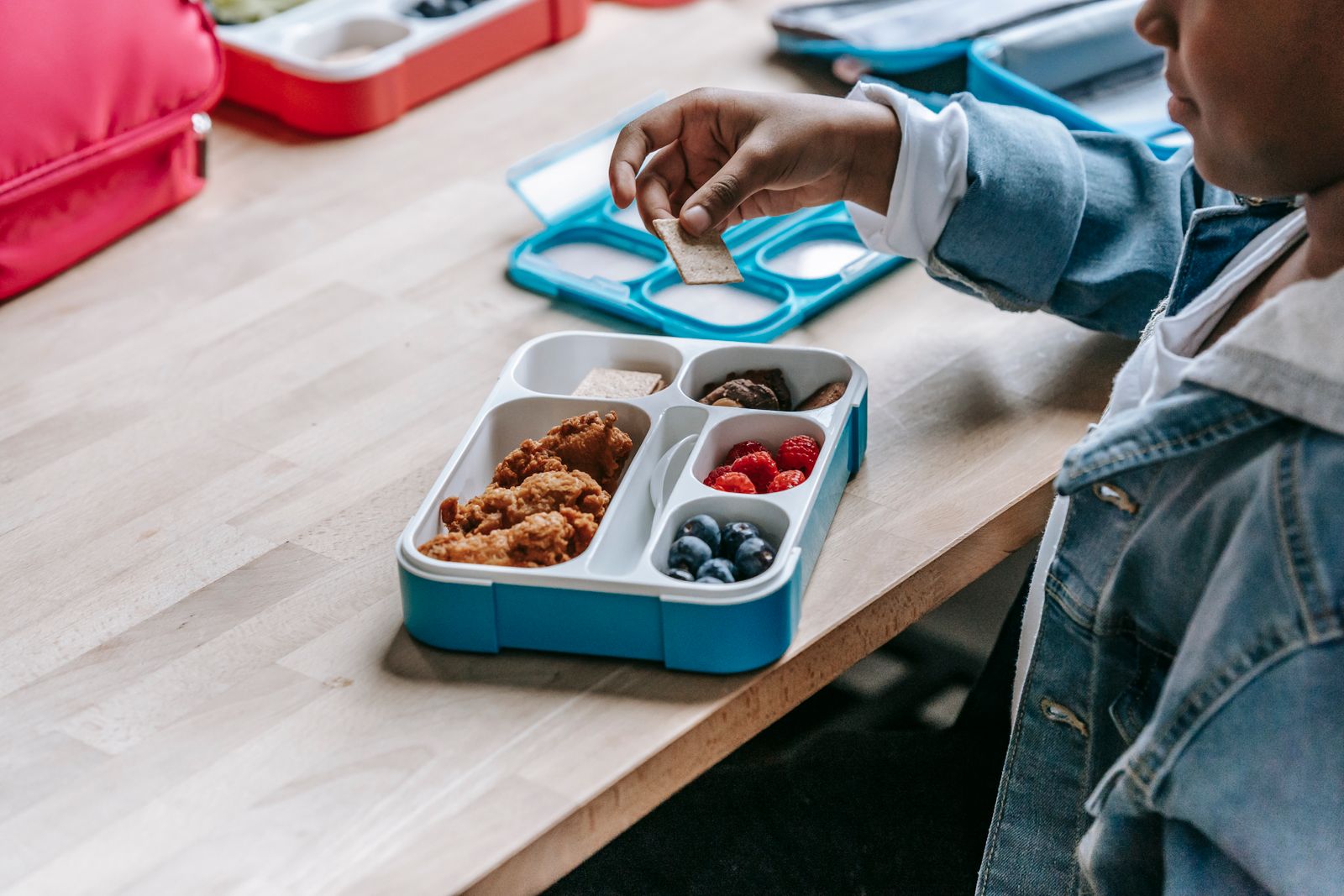 A child packing a bento lunchbox at the kitchen table